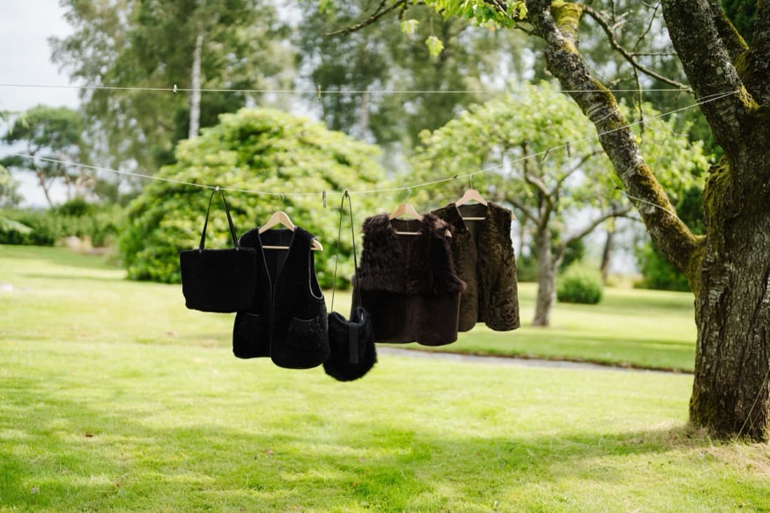Sheepskin vests and a fur bag hanging from a line between garden trees