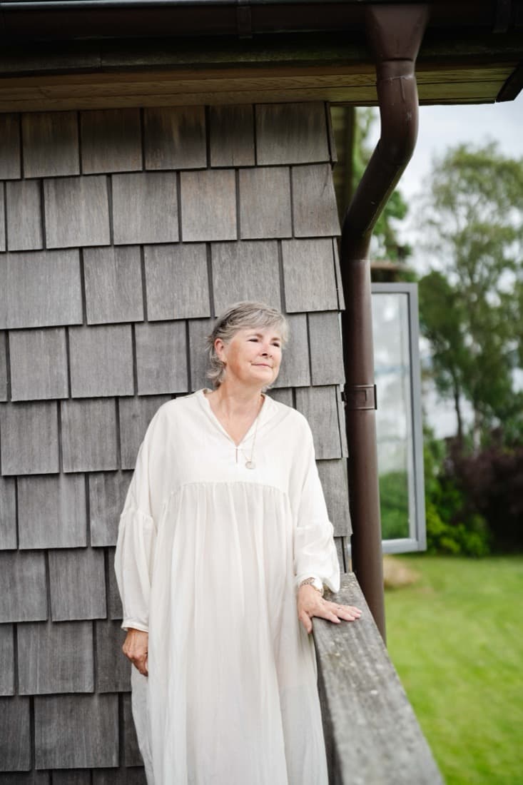 Birgitta standing beside a weathered timber cabin in the Swedish countryside